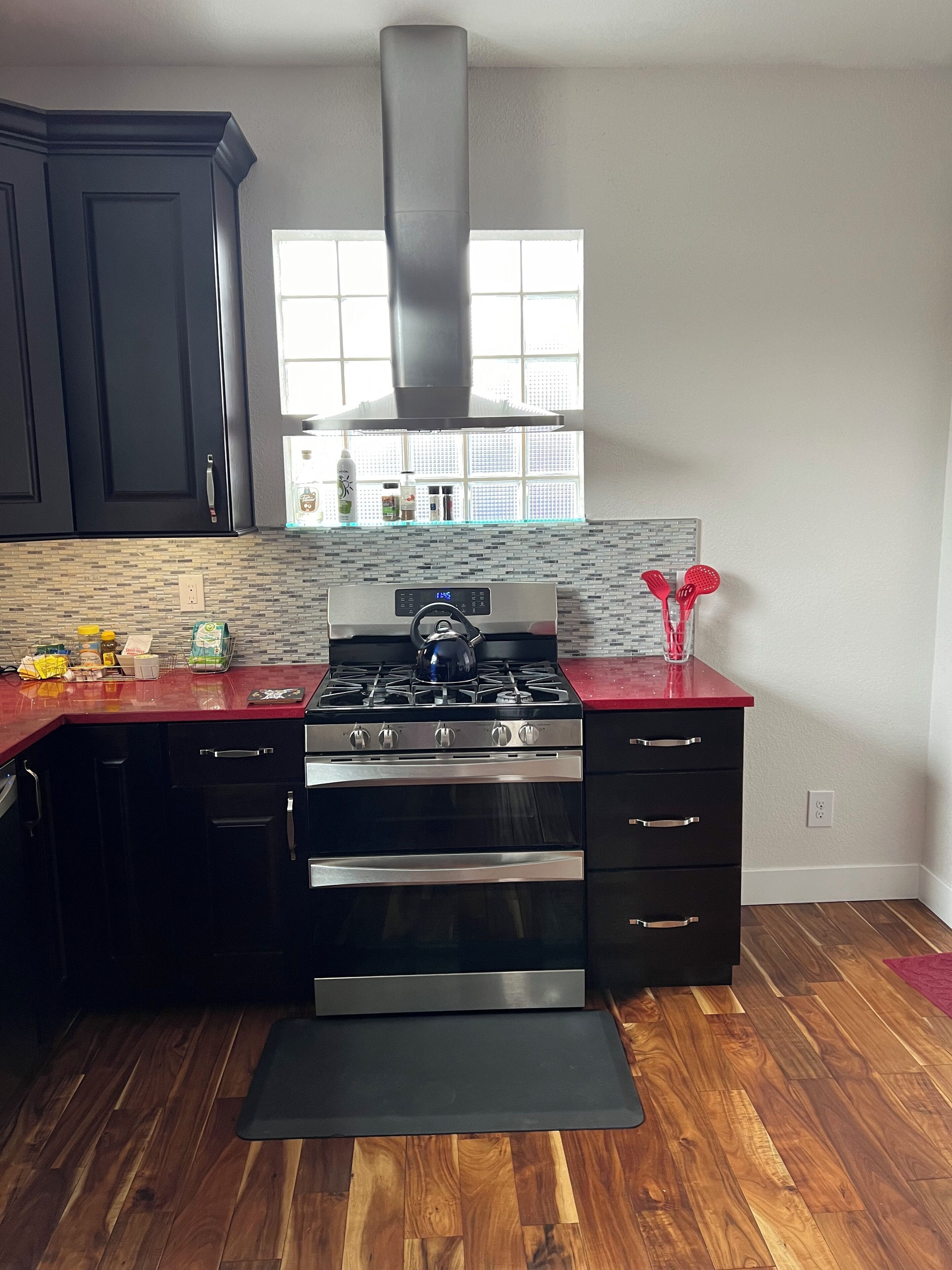 A kitchen with dark cabinets, a stainless steel stove, and a red countertop.