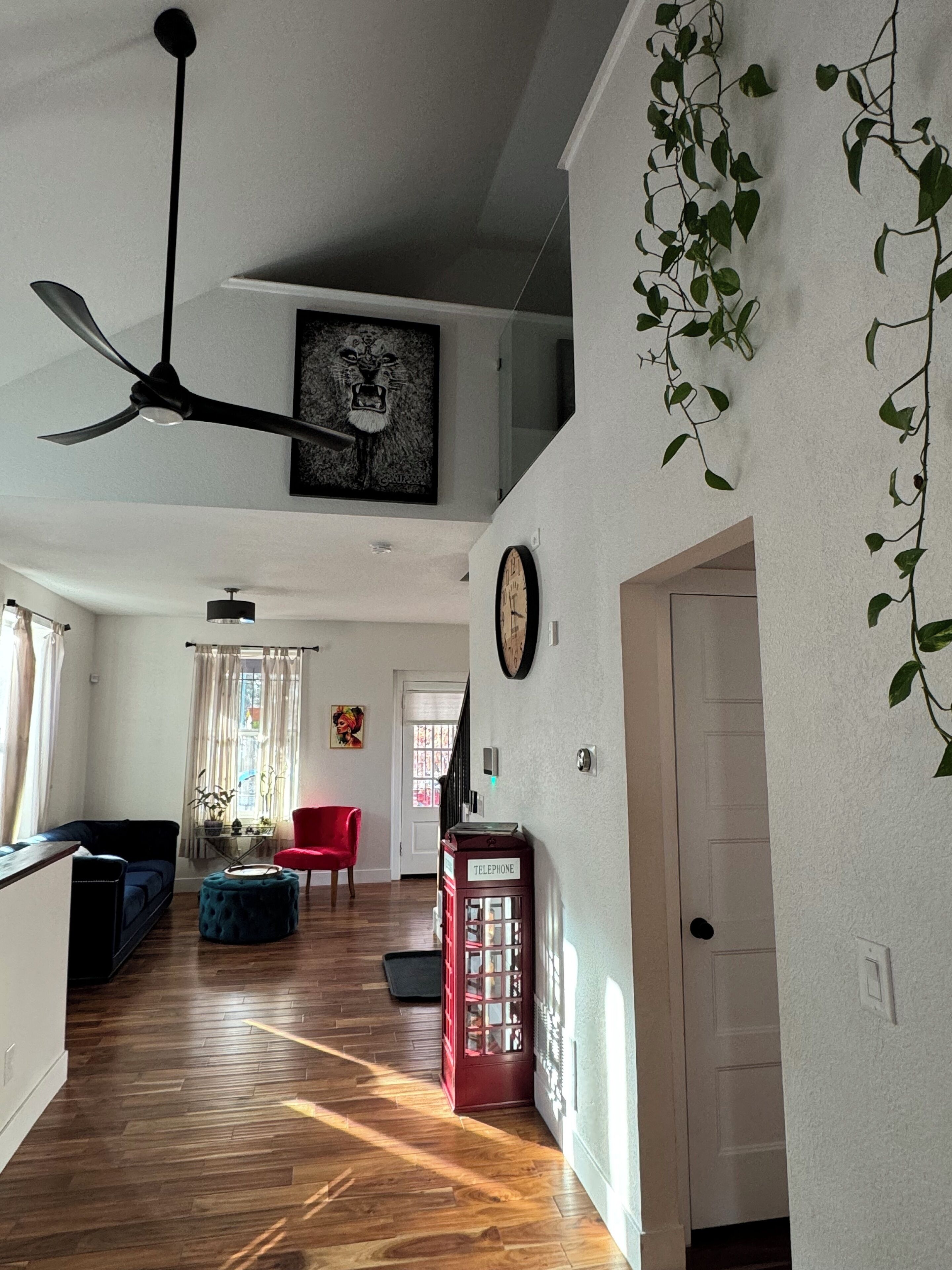 A spacious living area with a wooden floor, a ceiling fan, a red telephone booth, and a staircase leading to an upper level.
