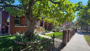 A residential street with brick houses, a tree-lined sidewalk, and a metal fence. - Cozy, custom bungalow in the heart of the Sante Fe Art District! (Denver)