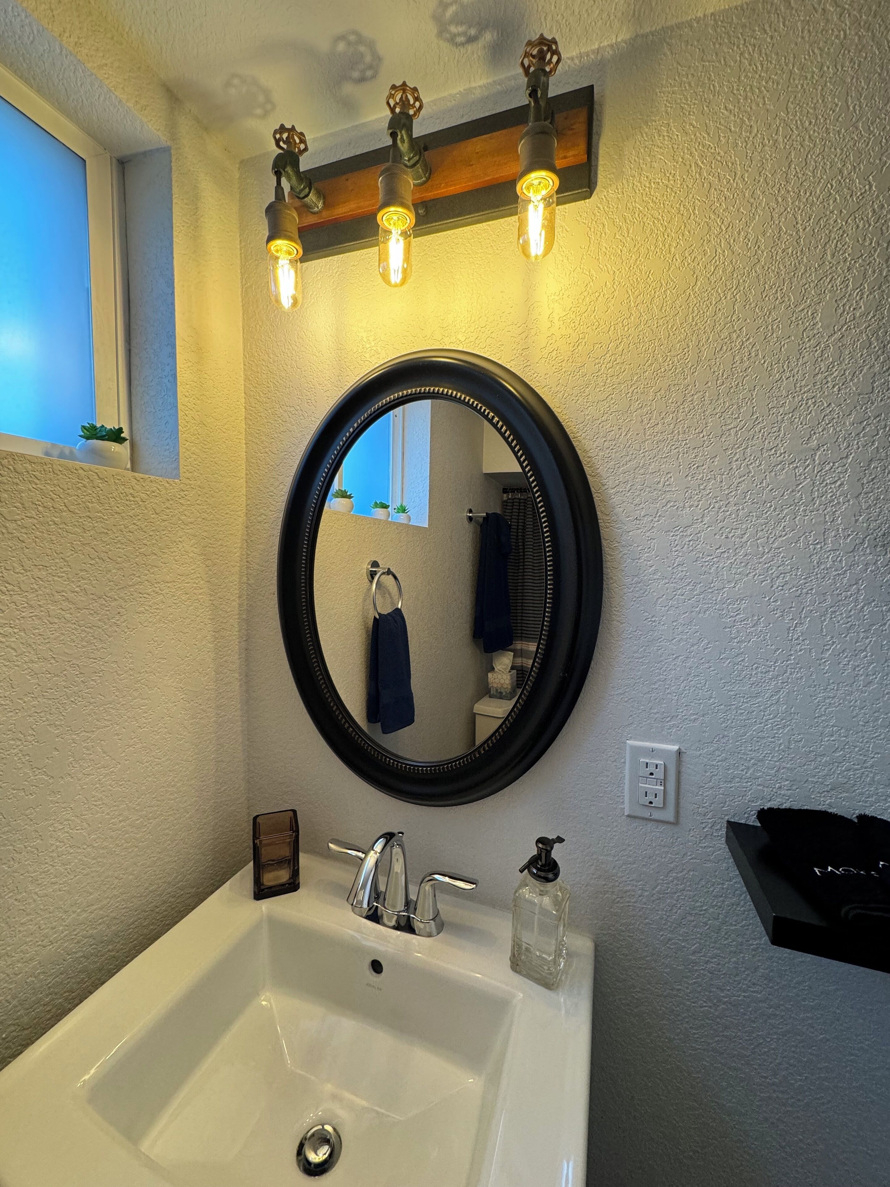 Een badkamer met een wit wastafelmeubel, een ronde spiegel en een lamp boven de spiegel.