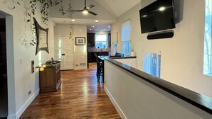 A spacious living area with hardwood flooring, a ceiling fan, and a TV mounted on the wall. - Cozy, custom bungalow in the heart of the Sante Fe Art District! (Denver)