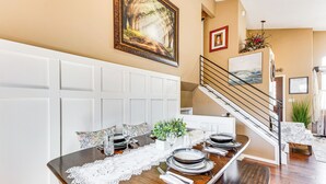 Un comedor con una mesa de madera preparada para seis personas, un banco blanco y una escalera que sube a un nivel superior.