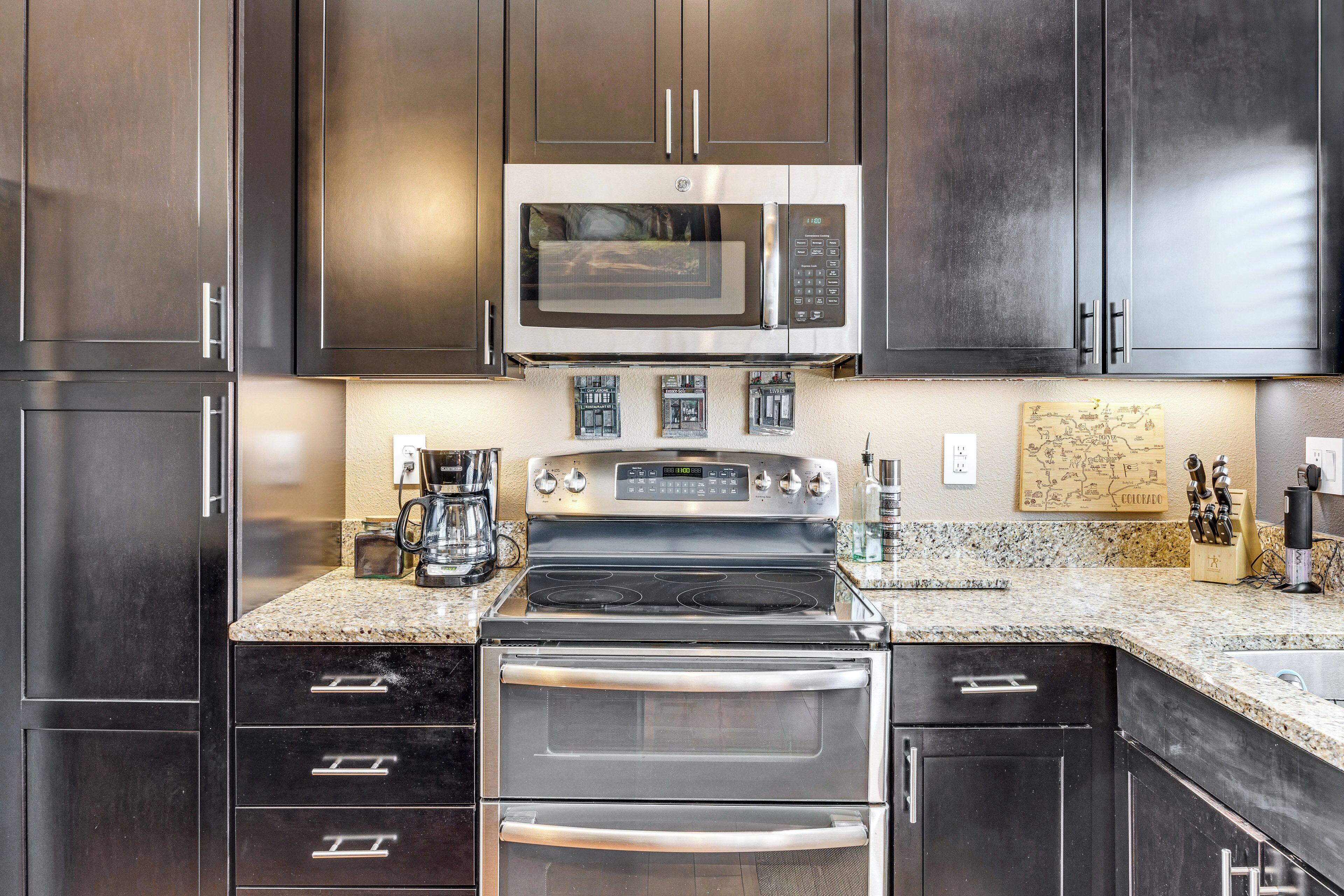 A modern kitchen with dark cabinetry, a stainless steel microwave, a gas stove, and a built-in oven.