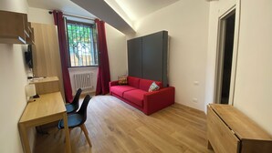 A modern room with a wooden desk, a red sofa, and a large TV screen. - Under Trastevere stars - Live like a local on Gianicolo hill! (Roma)