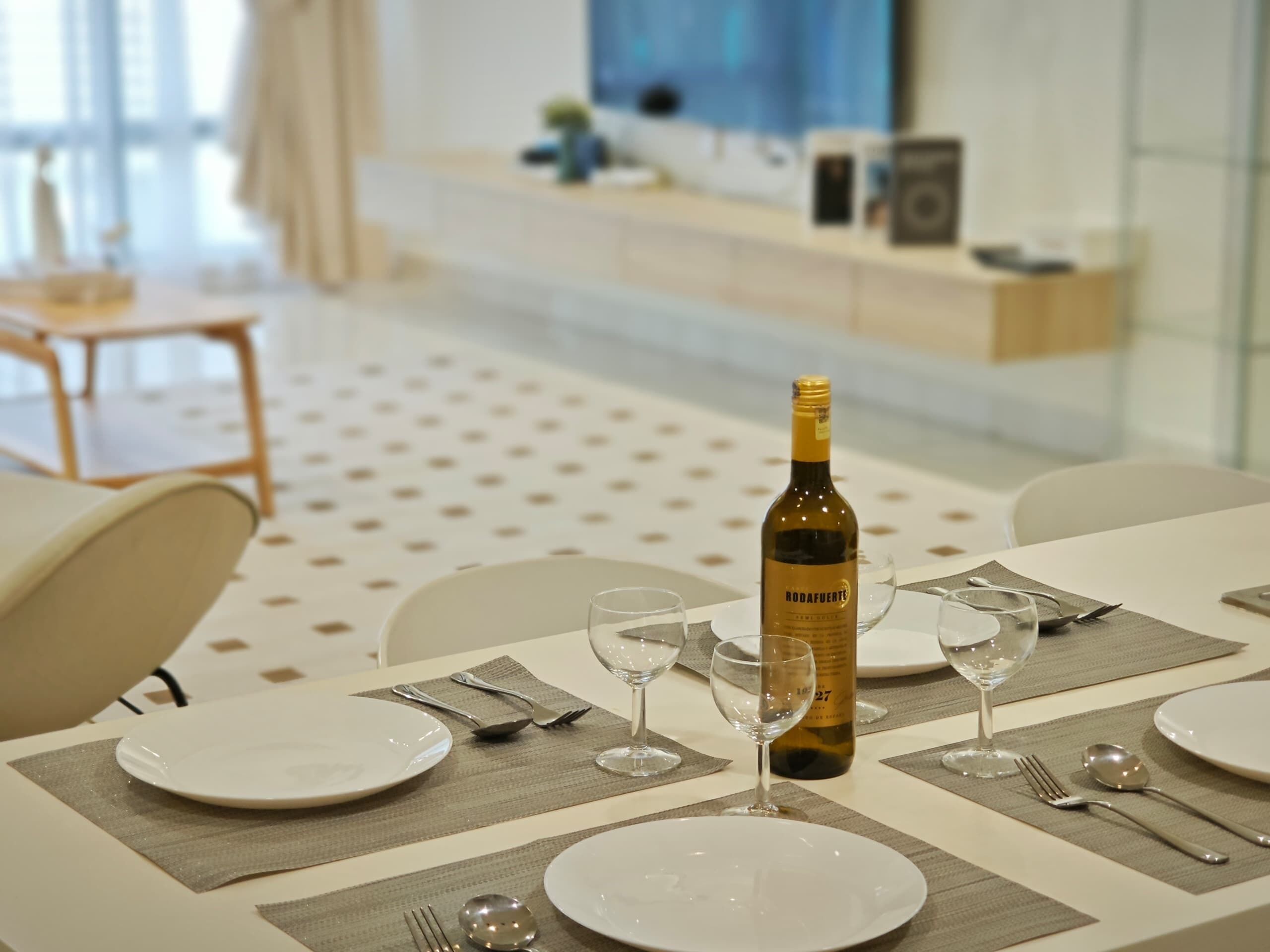 A dining area with a table set for four, including wine glasses, plates, and cutlery. A bottle of wine is placed on the table.