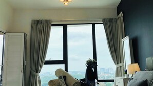 Un dormitorio con cama, una mesita de noche con lámpara, ventana con cortinas y vistas a la ciudad.