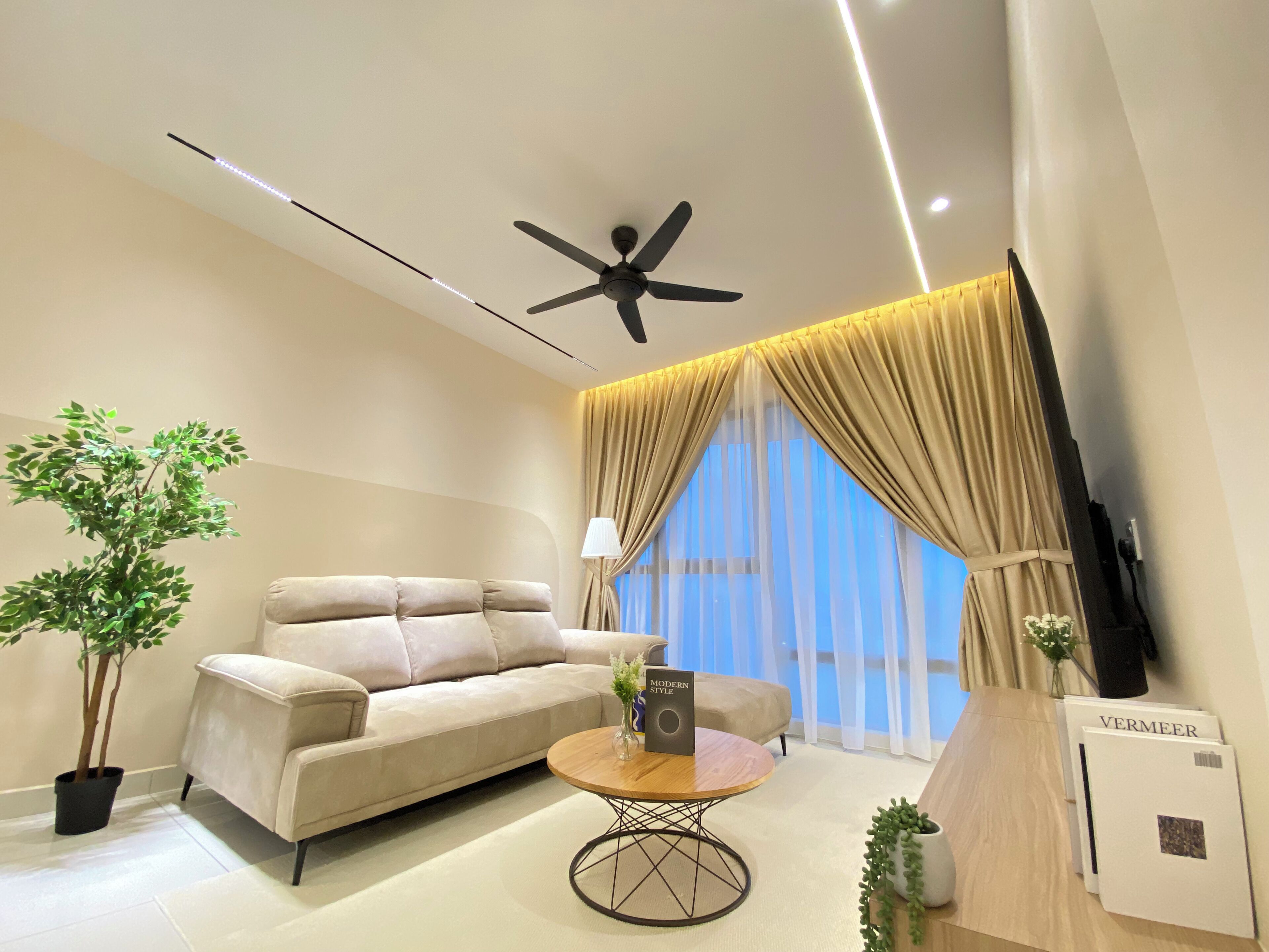 A modern living room with a sofa, a coffee table, a ceiling fan, and a TV.