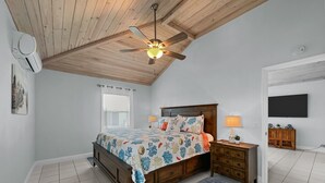Un dormitorio con techo de madera, una cama con colcha floral, una mesita de noche con lámpara y un televisor en la pared.