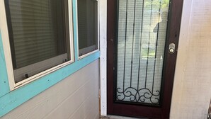 A corner of a building with a dark brown door with decorative metalwork, a window with blinds, and a paved entrance area. - Cozy, peaceful, very clean, you can work or just get away, weekly or monthly.   (Jacksonville)