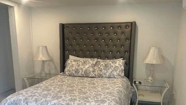 A bedroom with a tufted headboard, a floral-patterned bedspread, two bedside tables with lamps, and a striped rug. - Cozy, peaceful, very clean, you can work or just get away, weekly or monthly.   (Jacksonville)