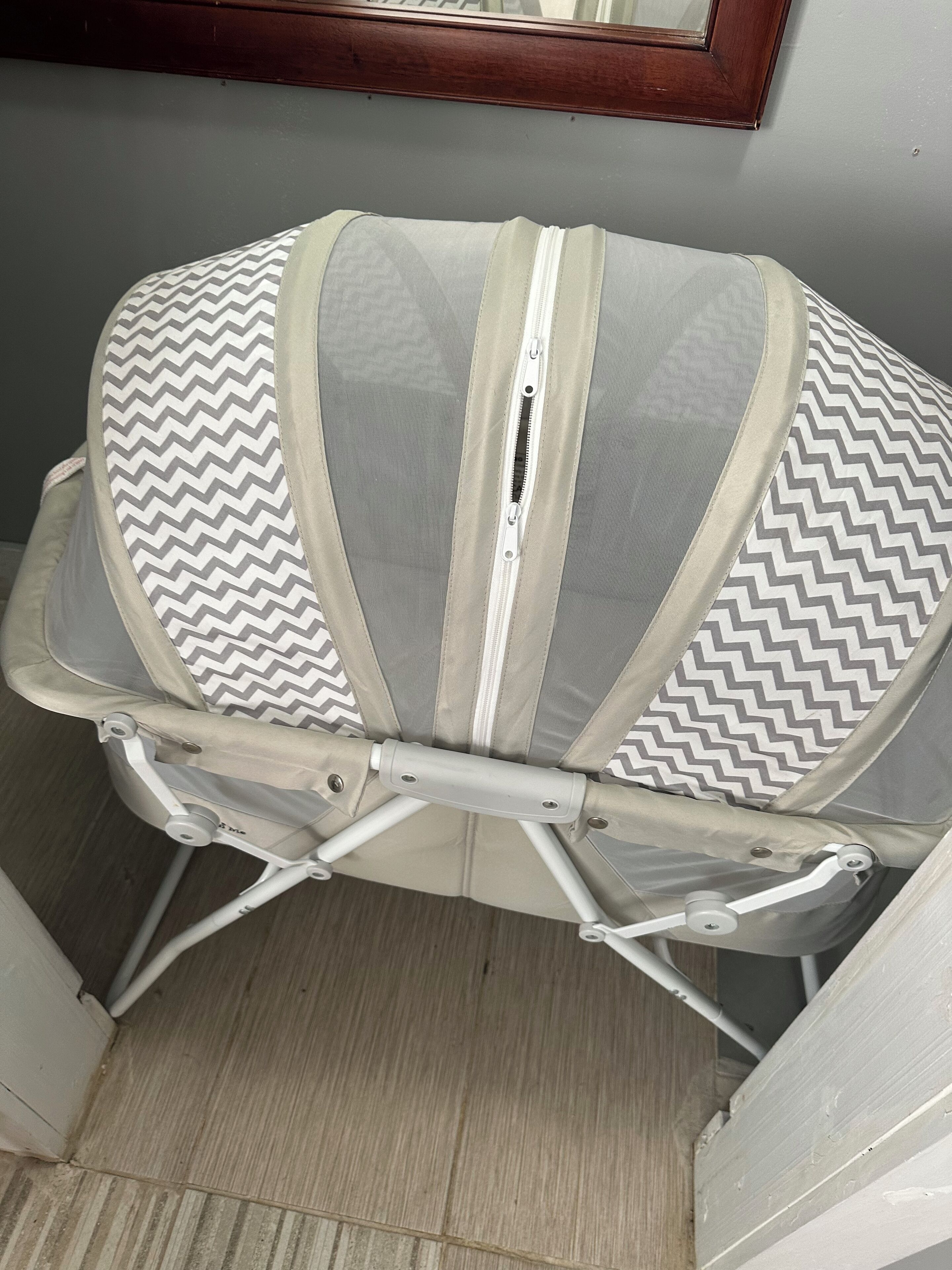 Une poussette pour bébé avec un motif à chevrons gris et blanc, un cadre blanc et un coussin de siège beige.