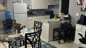 A compact kitchen with white cabinets, a refrigerator, a microwave, and a coffee maker. There is a dining table with chairs and a vase of flowers. - Cozy, peaceful, very clean, you can work or just get away, weekly or monthly.   (Jacksonville)