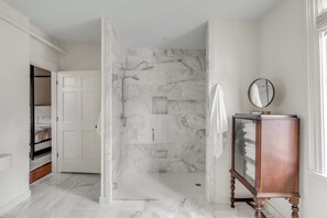 A modern bathroom with a glass-enclosed shower, marble flooring, a wooden vanity with a mirror, and a white towel hanging on the wall.