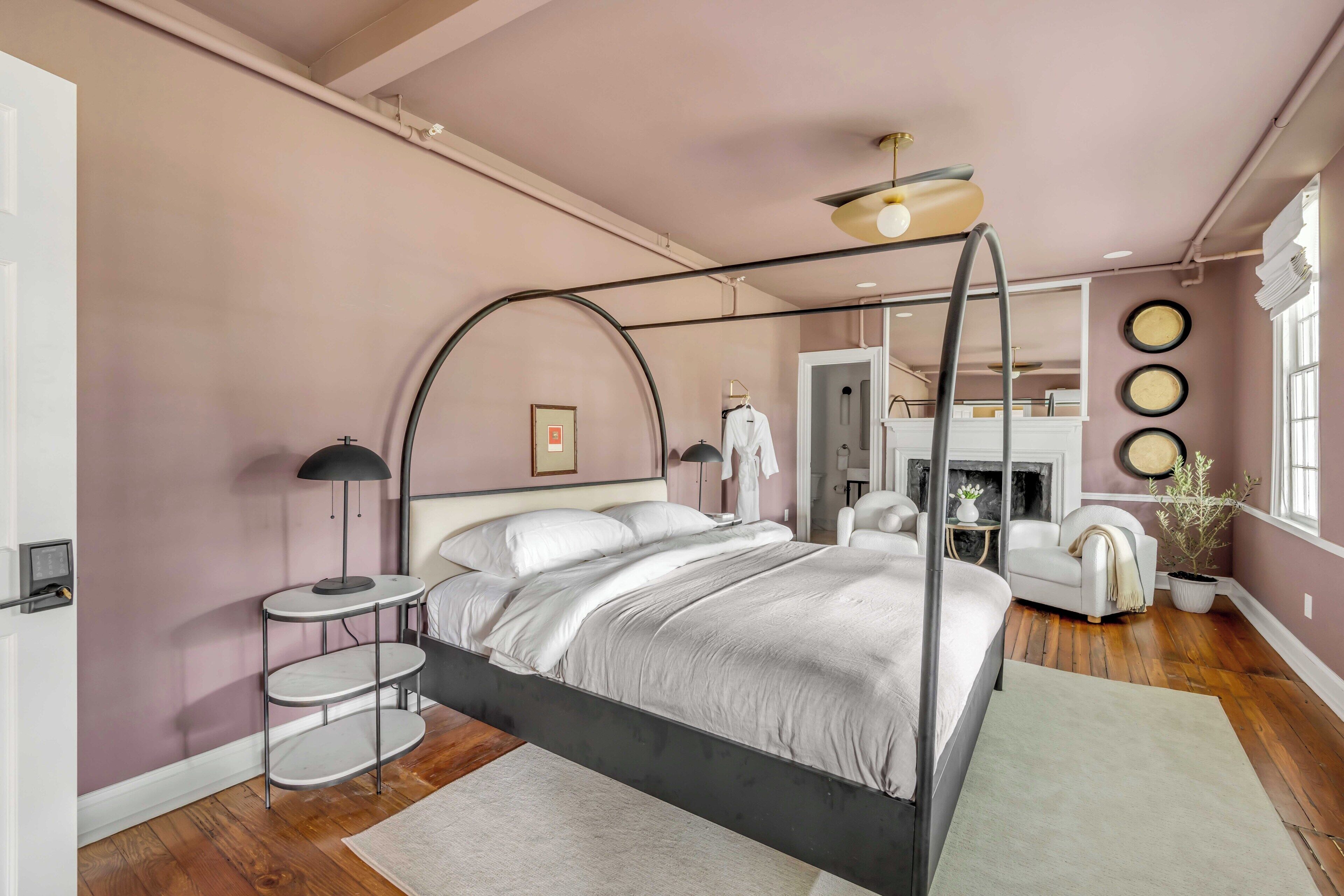 Un dormitorio con una cama con dosel, un espejo redondo, una mesita de noche y una planta en maceta.