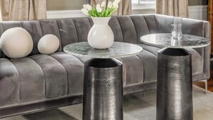 Uma sala de estar moderna com um sofá cinzento, uma mesa de centro redonda e dois vasos pretos.