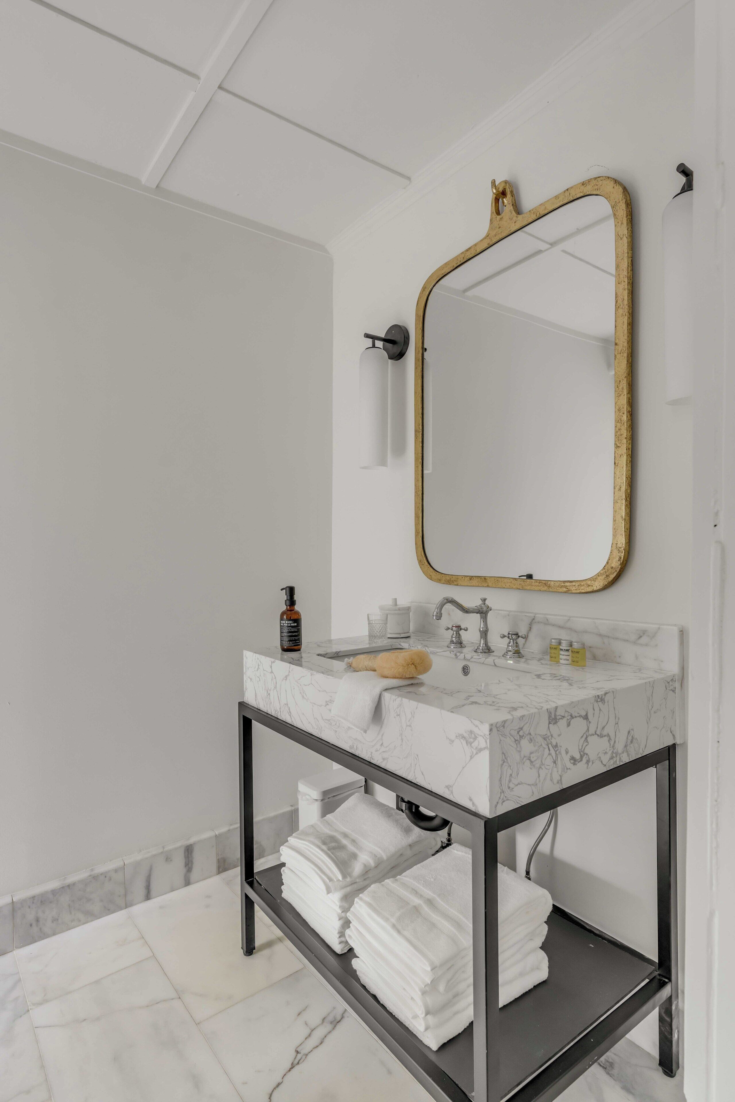 A bathroom with a marble sink, a gold-framed mirror, and a towel rack with folded towels.