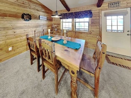 A wooden cabin interior with a dining table, chairs, a chandelier, and a door with a sign.
