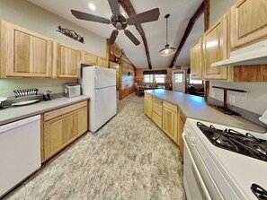 Une cuisine avec des meubles de rangement en bois, un réfrigérateur, une cuisinière et un ventilateur de plafond.