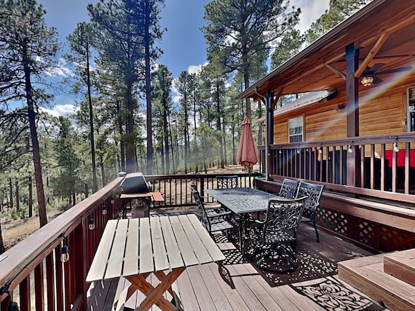 A wooden deck with a table and chairs, surrounded by tall trees. - 4 Bears 1 Cave by Ruidoso Vacation Rentals (Alto)