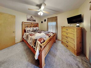 A bedroom with a wooden bed, a ceiling fan, a TV on a wooden dresser, and a window with curtains. - 4 Bears 1 Cave by Ruidoso Vacation Rentals (Alto)
