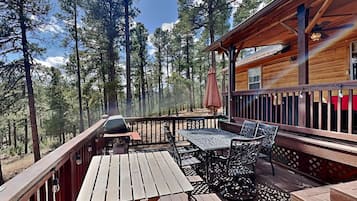 A wooden deck with a table and chairs, surrounded by tall trees.