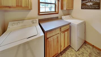 A laundry room with wooden cabinets, a washing machine, a dryer, and a window with a checkered curtain.