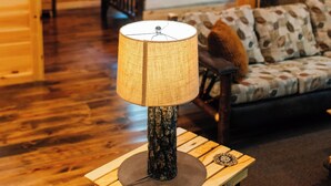 A cozy wooden cabin interior with a bed, a sofa, a lamp, and a chandelier.