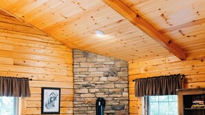 A cozy cabin interior with wooden walls, a stone fireplace, a sofa, a table, and a lamp.