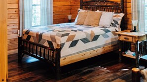 A wooden cabin bedroom with a bed, a chandelier, and a wooden floor.