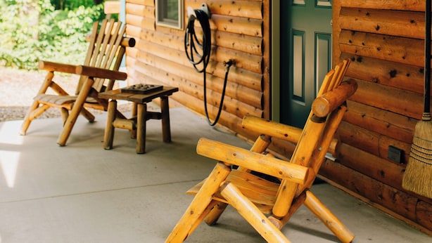 A wooden cabin with two wooden chairs and a broom leaning against the wall.