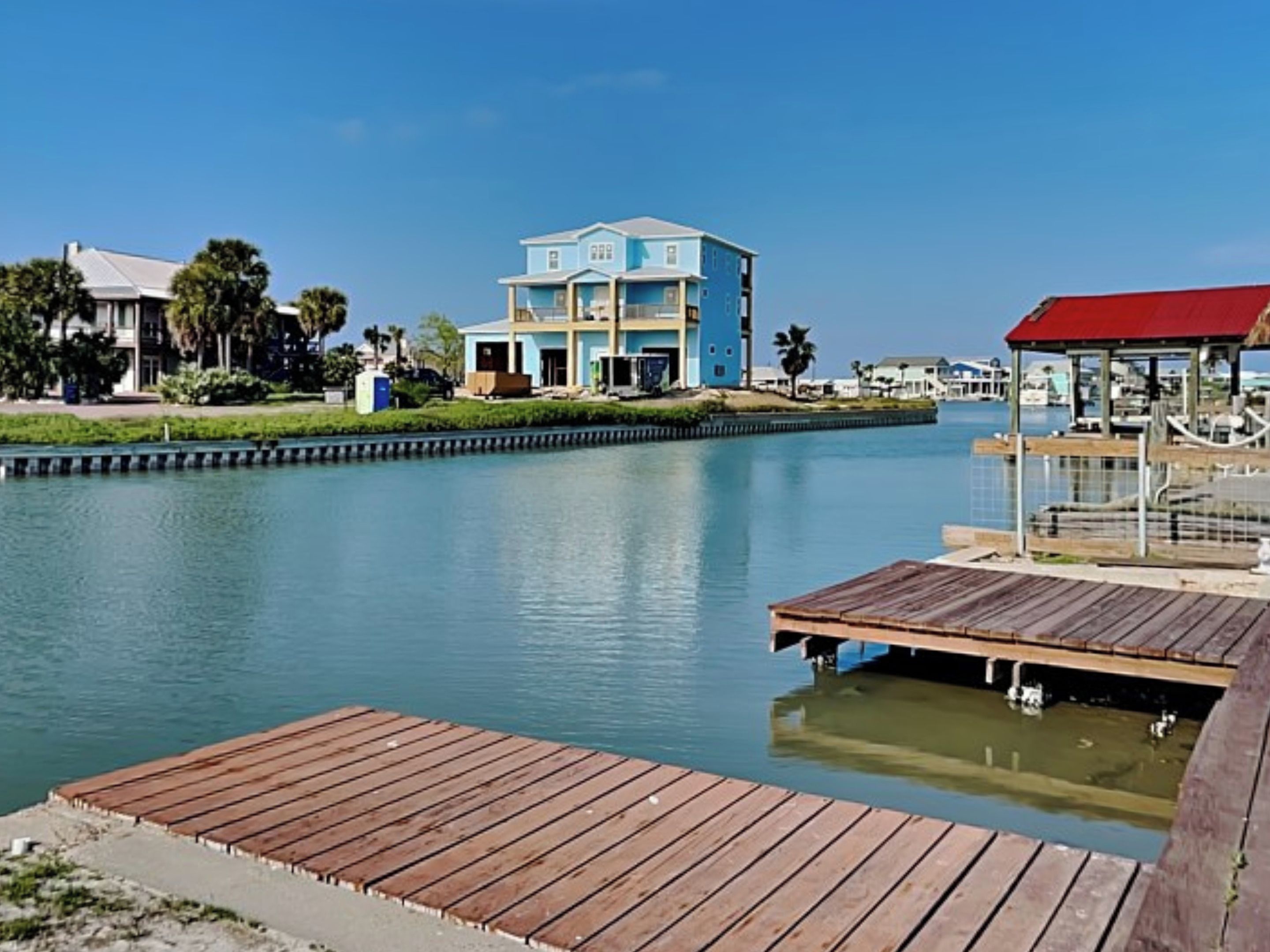 A waterfront property with a large blue house, a wooden dock, and a small pier with a red roof.