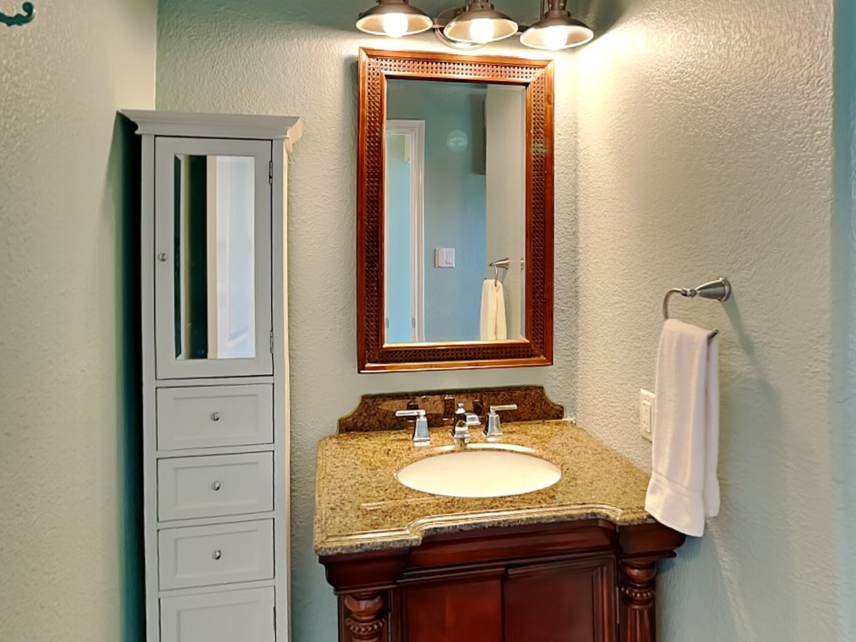 A bathroom with a white cabinet, a granite countertop sink, and a large mirror with a wooden frame.