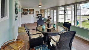 Eine überdachte Terrasse mit rundem Tisch und Stühlen, einem Grill und Blick auf den Garten.