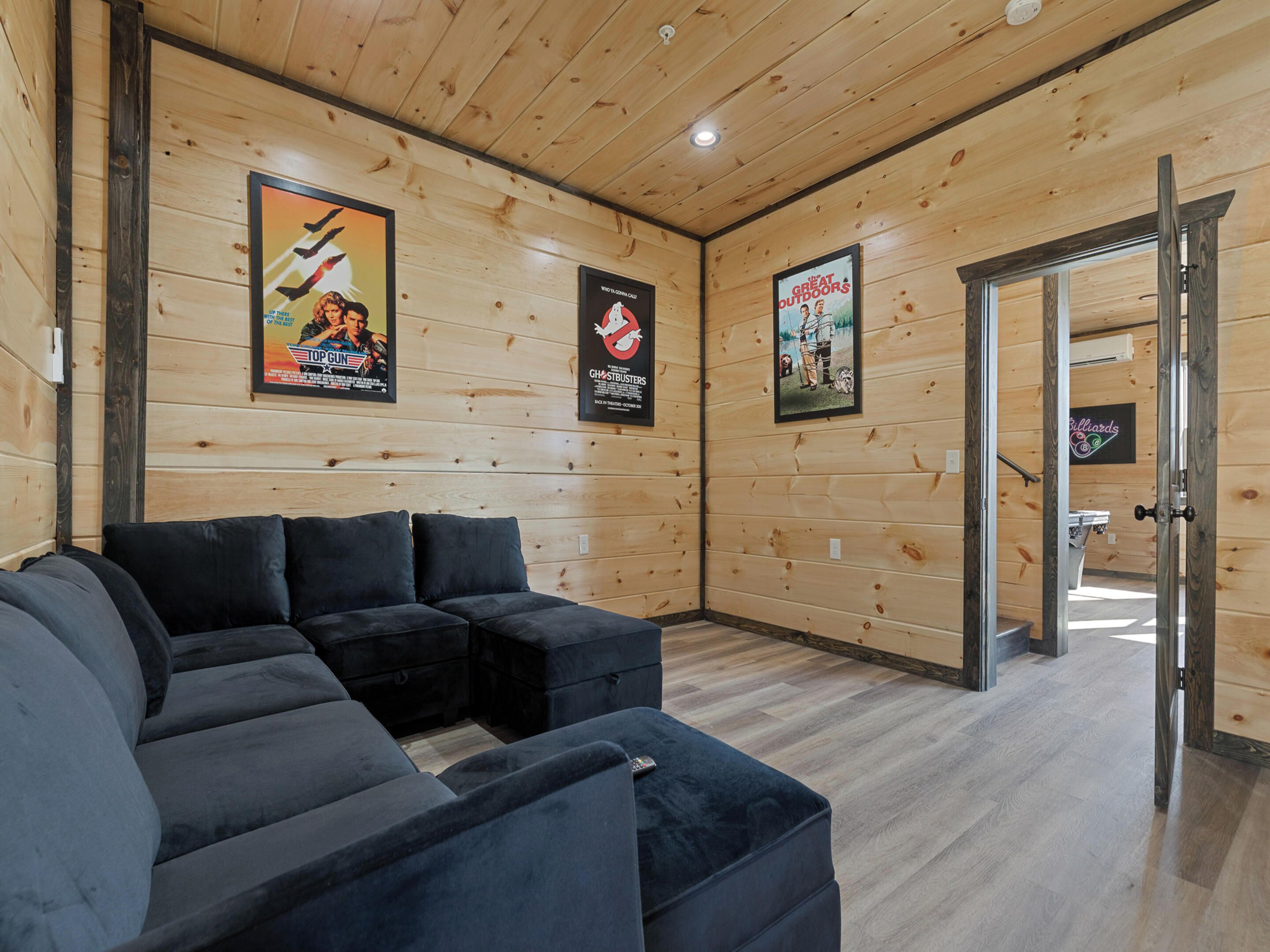 A cozy room with a sectional sofa, wooden walls, and framed movie posters.