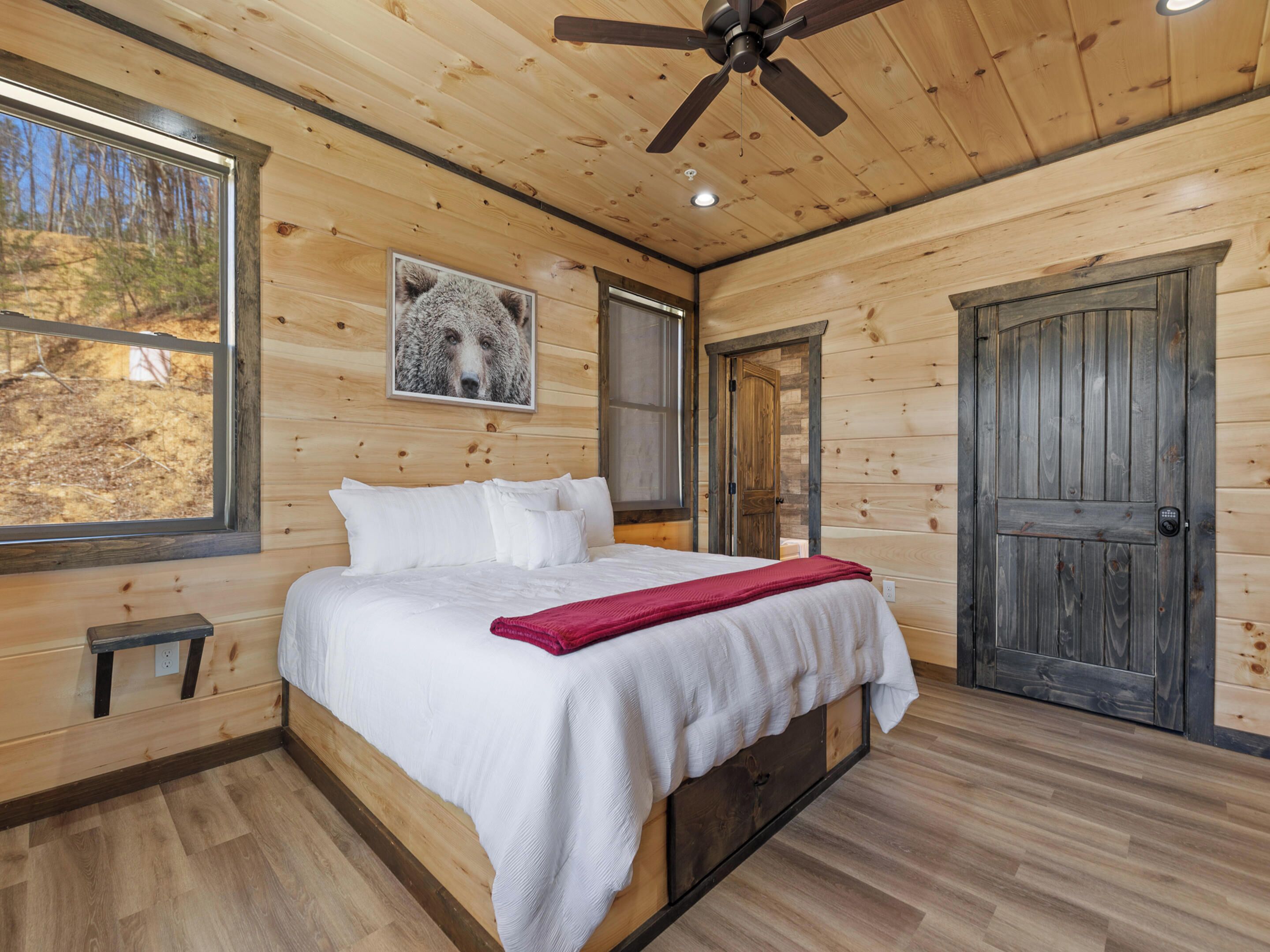 A wooden cabin bedroom with a bed, a ceiling fan, and a large window.