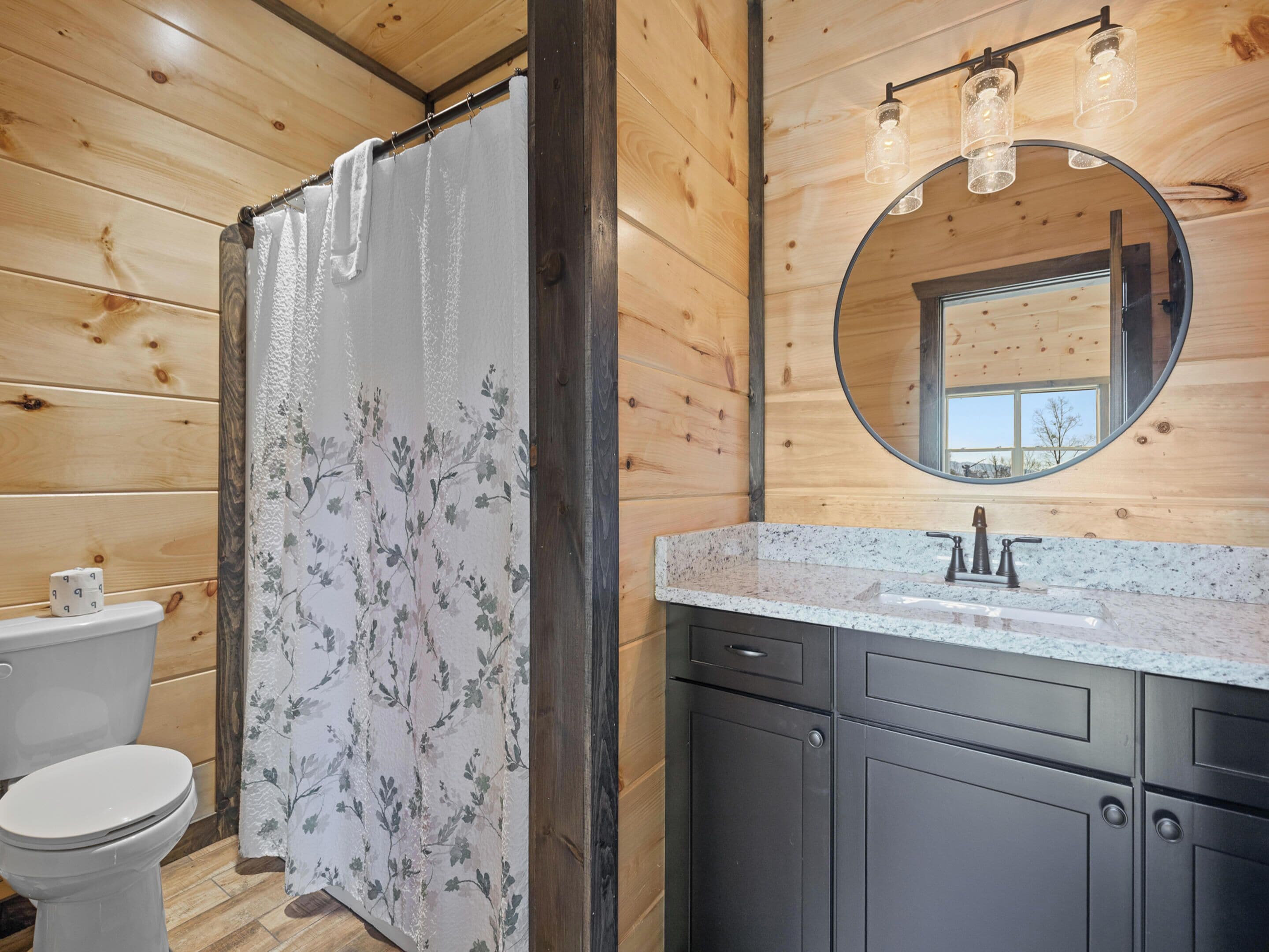 A wooden interior with a shower curtain, toilet, sink with a mirror, and cabinets.