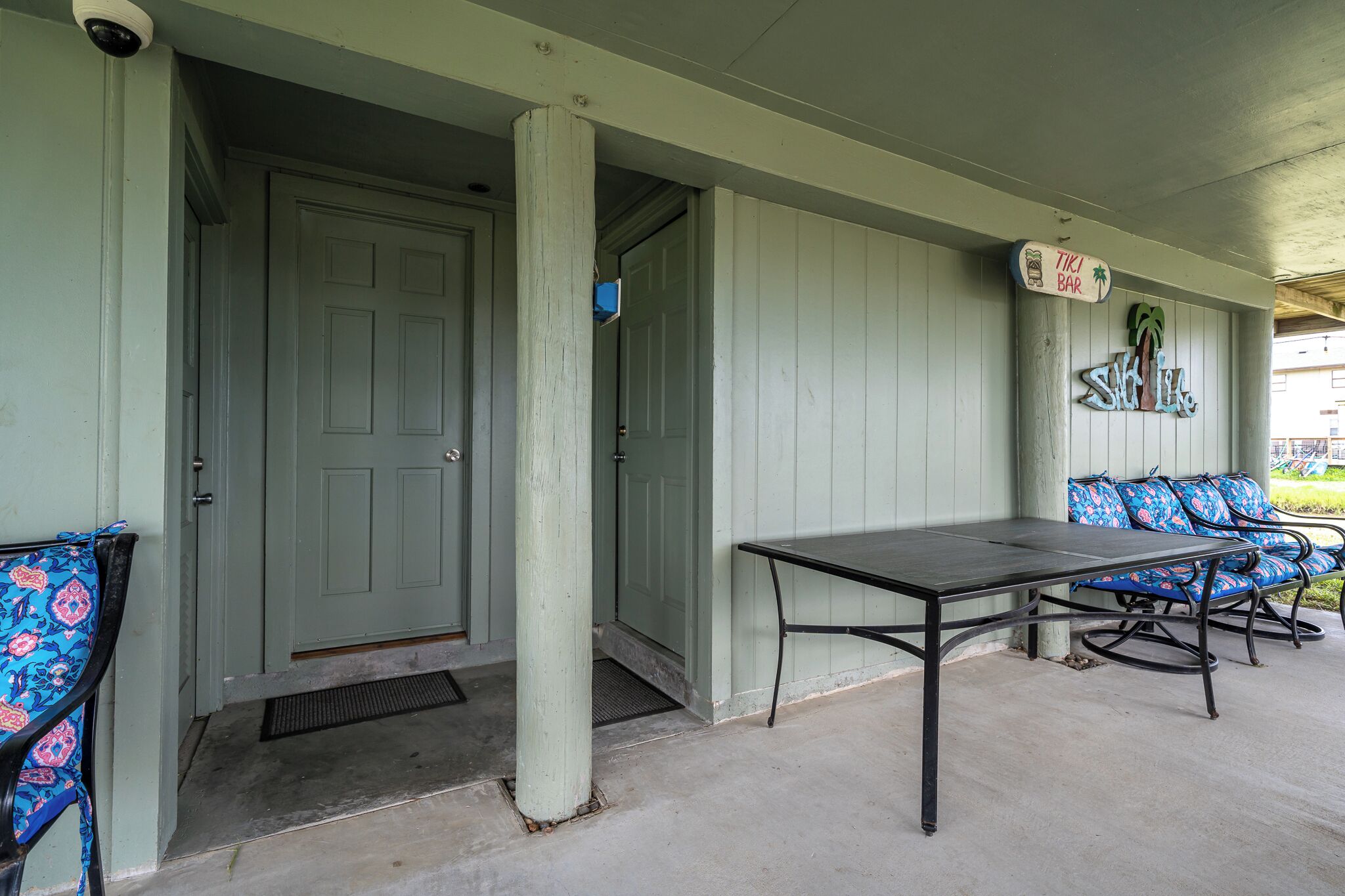 A covered porch with a table and chairs, a door, and a sign indicating a tiki bar.