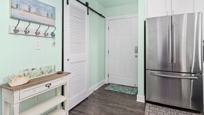 Une cuisine équipée d’un réfrigérateur en acier inoxydable, d’une porte blanche et d’un porte-manteau mural avec des crochets.