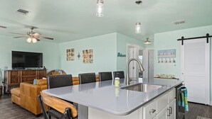 Une cuisine moderne avec un îlot central, un coin repas avec des chaises, un canapé et un téléviseur dans le salon.
