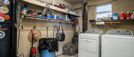 Une buanderie équipée d’un lave-linge, d’un sèche-linge et d’étagères où sont rangés les produits d’entretien.