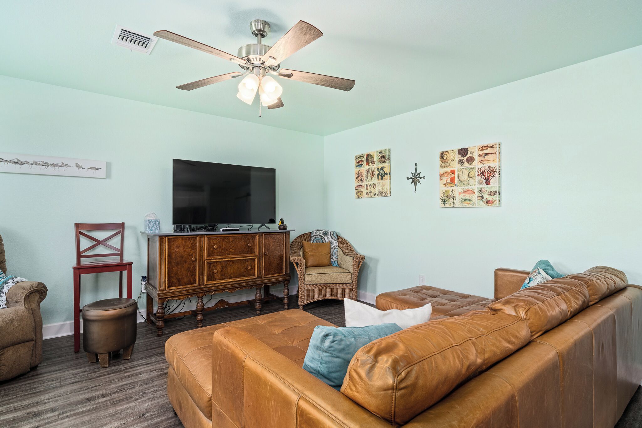 A living room with a brown leather sofa, a wooden cabinet, a television, and wall art.