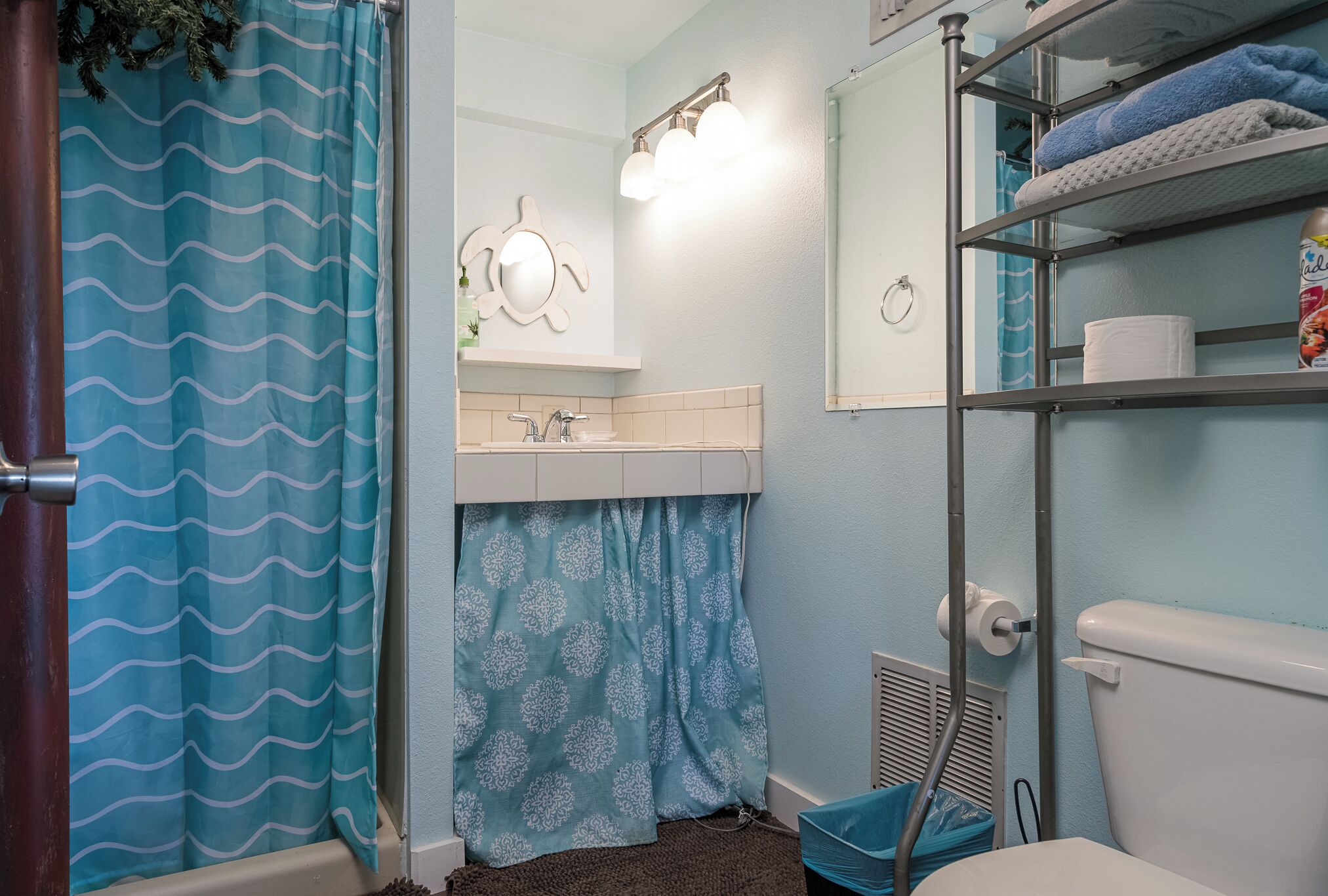 A bathroom with a shower curtain, a sink, a toilet, and a shelf with towels.