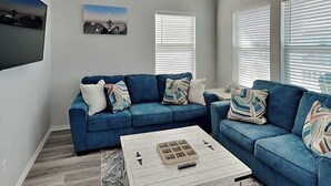 Ein Wohnzimmer mit einem blauen Ecksofa, einem Couchtisch und einem an der Wand befestigten Flachbildfernseher.