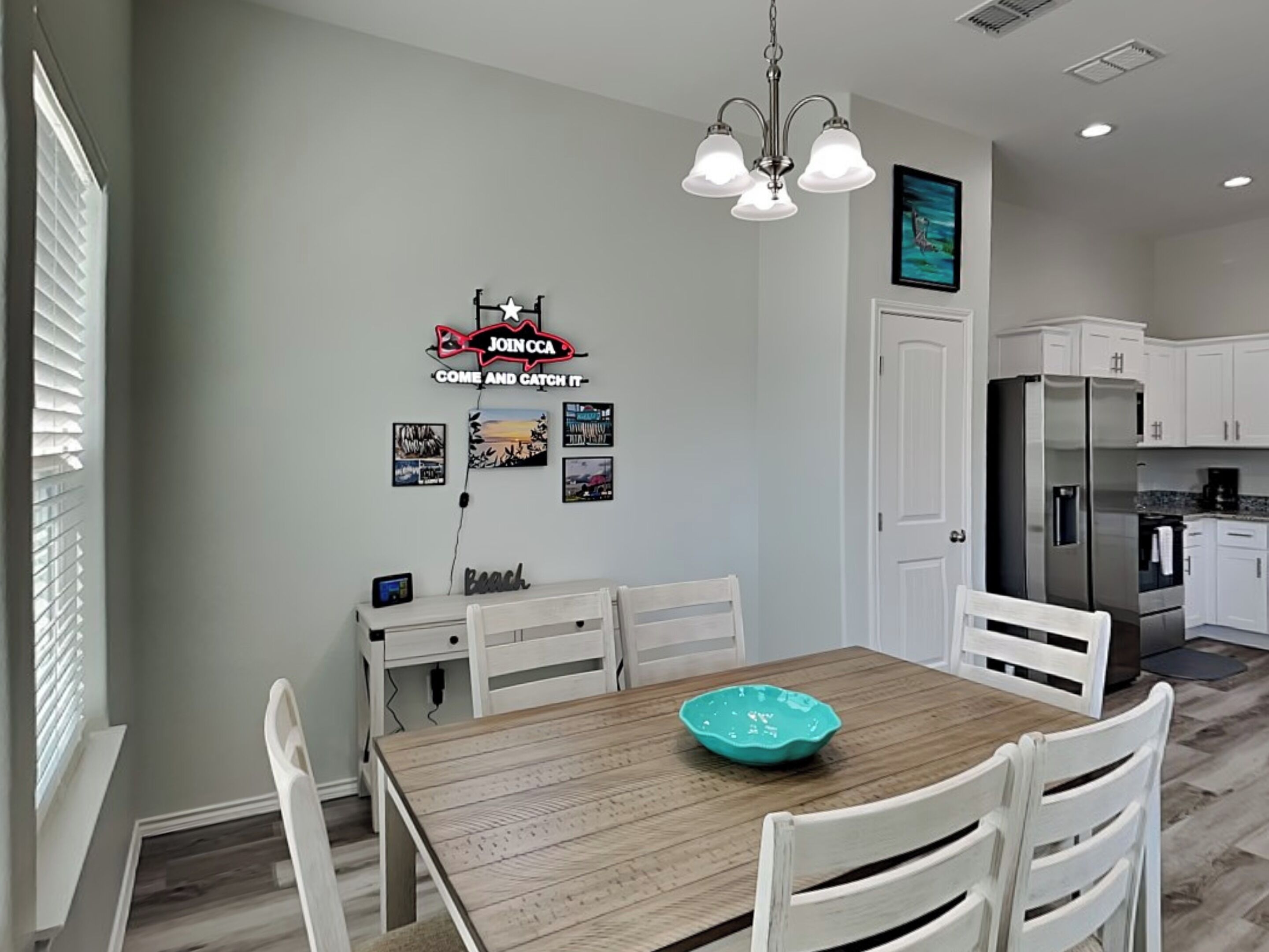 Une cuisine moderne avec des meubles blancs, une table à manger en bois et un bol de couleur turquoise.