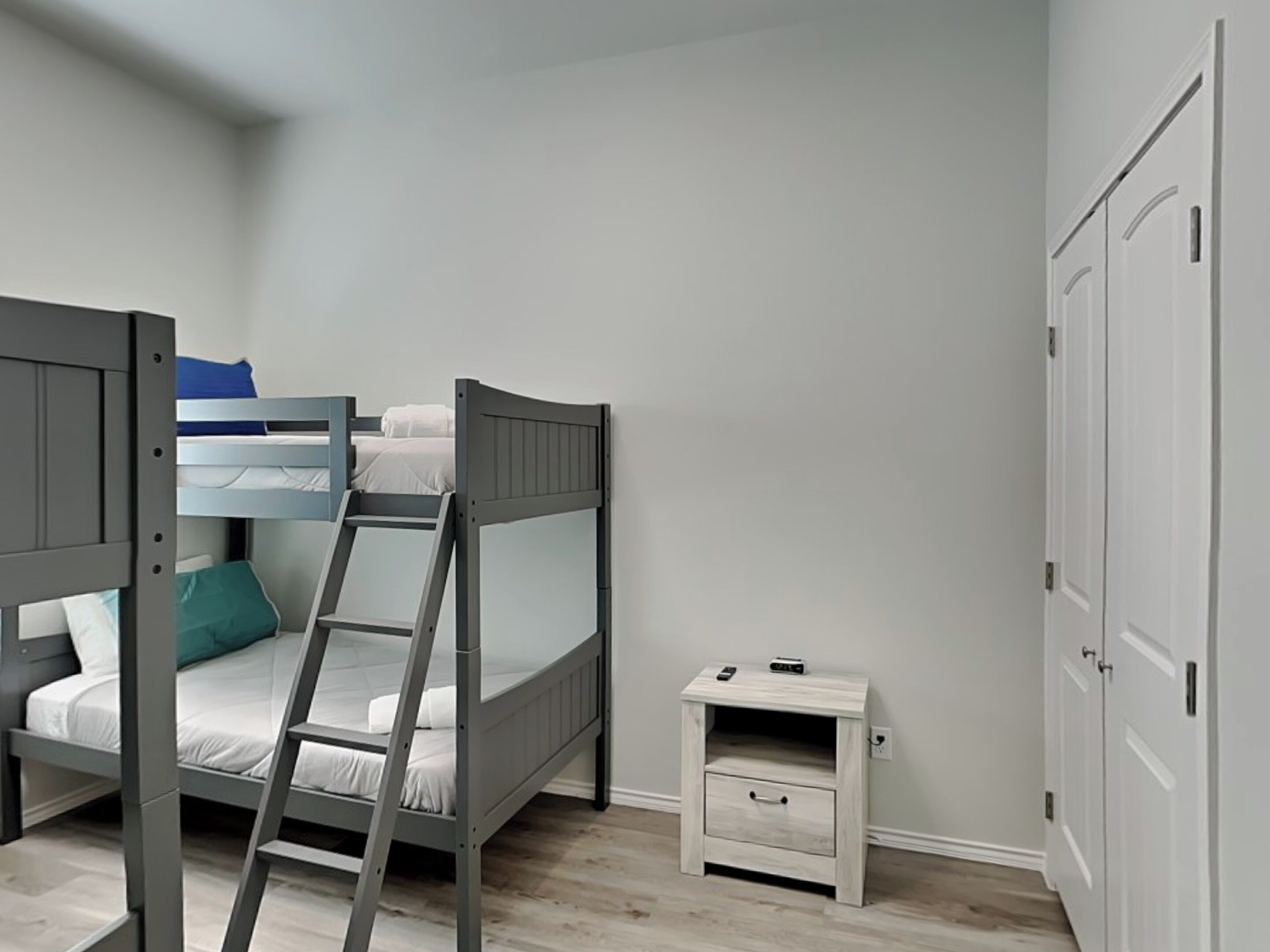 A bedroom with a bunk bed, a bedside table with a drawer, and a wardrobe.
