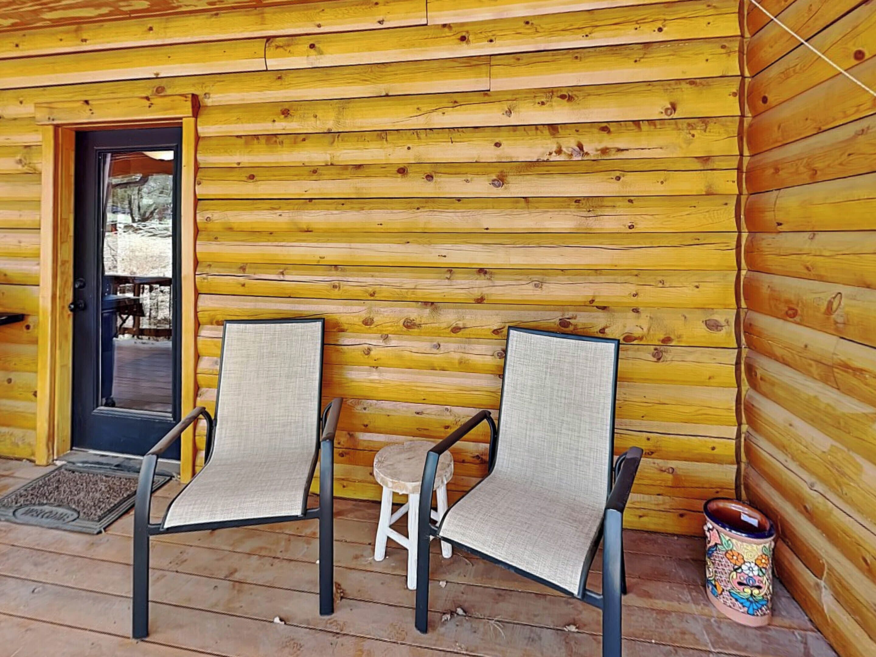 A wooden cabin with two chairs and a small stool on the porch.