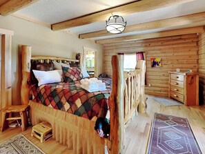 A cozy wooden cabin bedroom with a large bed, a wooden dresser, and a small stool. - Double Eagle Manor by Ruidoso Vacation Rentals (Alto)