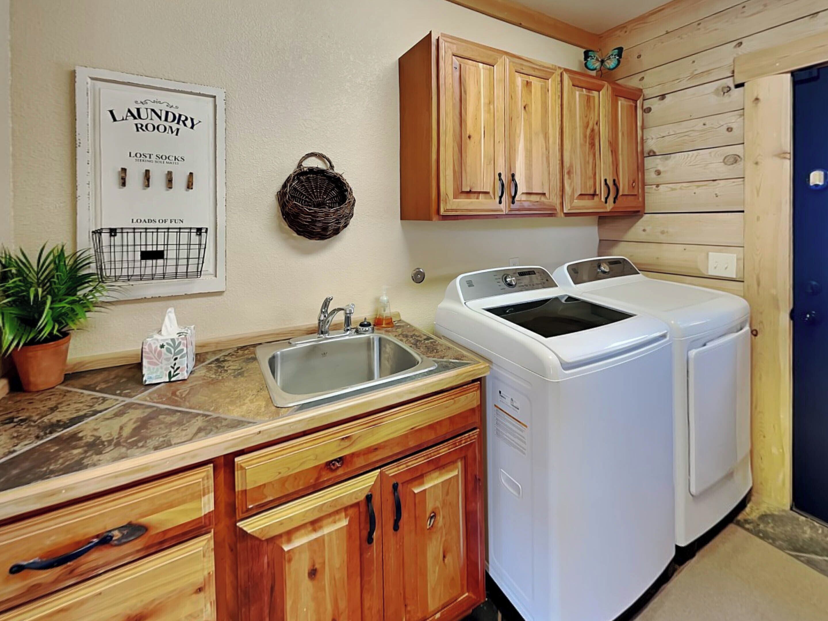 A laundry room with wooden cabinets, a washing machine, a sink, and a potted plant.