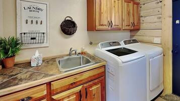 A laundry room with wooden cabinets, a washing machine, a sink, and a potted plant.