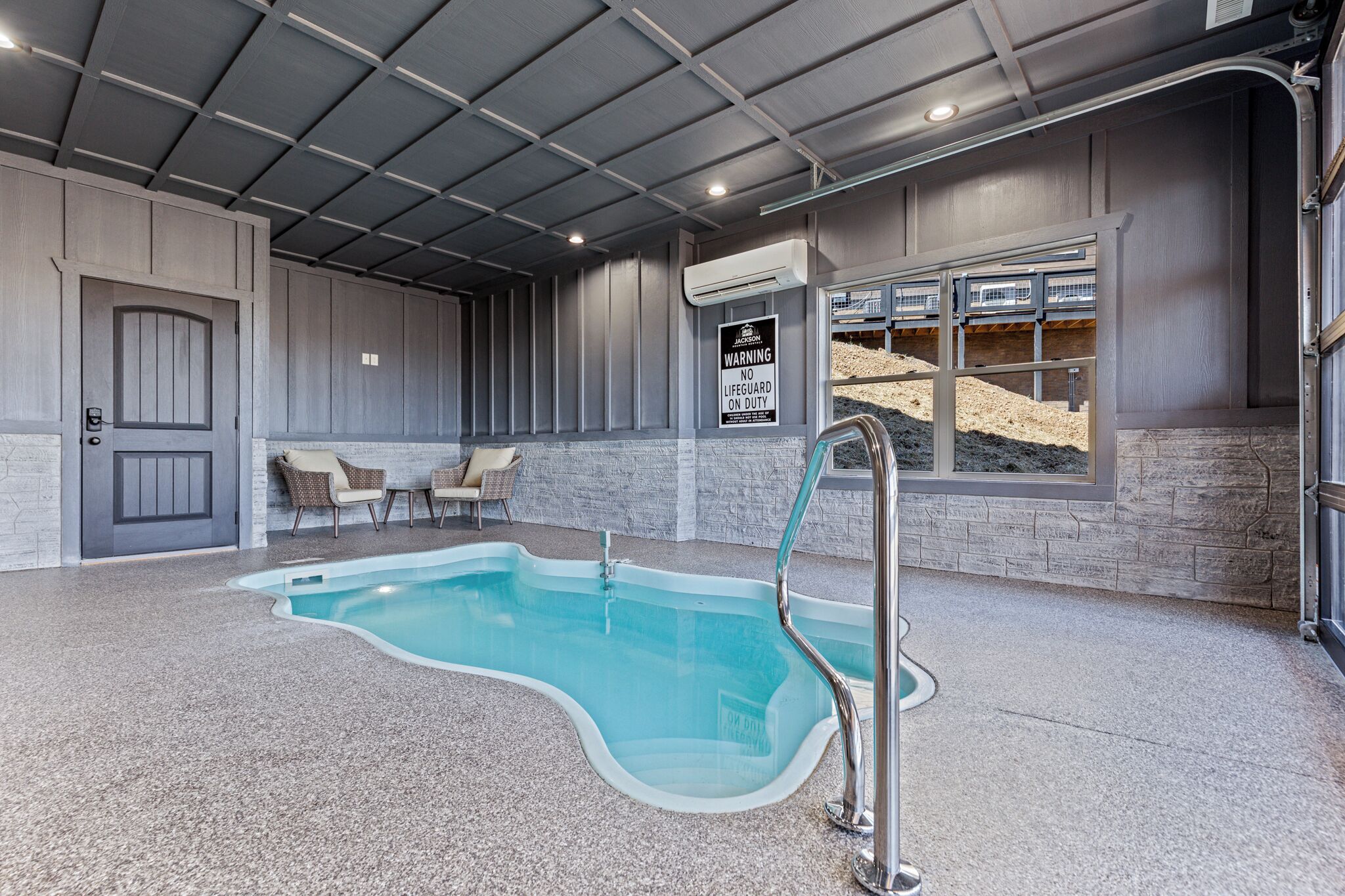 Una piscina interior amb una vista clara de la zona de la piscina, un senyal de socorrista i una finestra amb vista a una zona de construcció.
